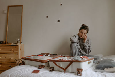 Woman calling taxi before going to airport, open suitcase on the bed