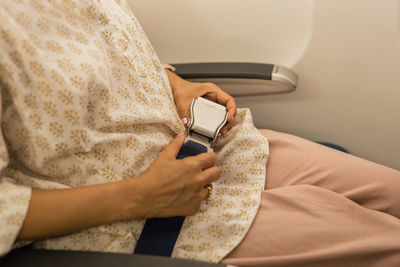 Woman fastens seat belt while sitting in a passenger airplane chair by the window.