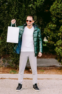 Full length of man holding shopping bag standing against plants