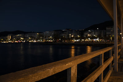 Illuminated buildings by river against sky at night