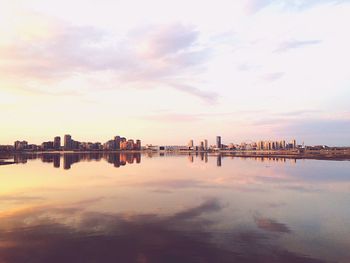 Scenic view of river by buildings against sky during sunset