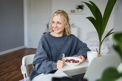 Portrait of young woman using mobile phone while sitting at home