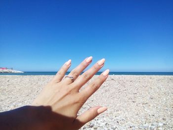 Close-up of woman hand on beach against clear blue sky