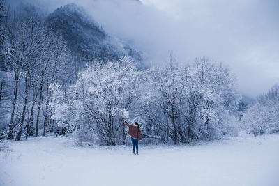 Rear view of woman standing on snow covered land by trees