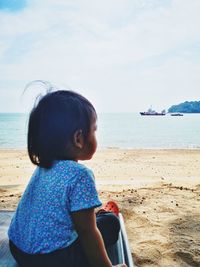 Girl sitting at beach against sky