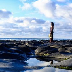 Woman standing on rock by sea against sky