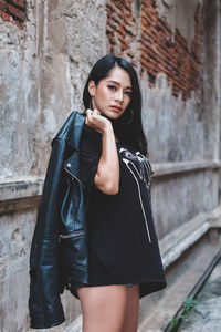 Portrait of beautiful young woman standing against brick wall