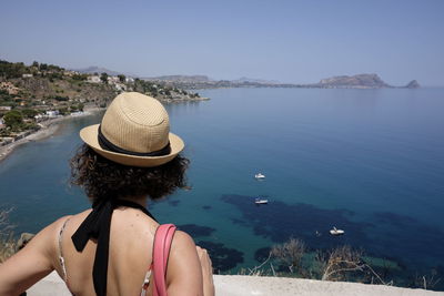 Rear view of woman wearing straw hat on cliff by sea at capo zafferano