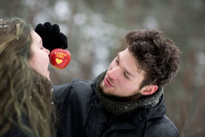 Close-up of couple having apple with text during winter