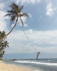 Woman playing on swing over beach against cloudy sky