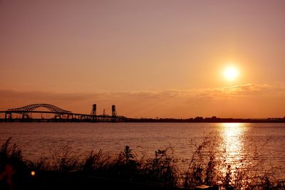 Silhouette bridge over river against sky during sunset