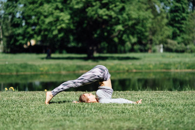 Full length of young woman exercising by pond on field