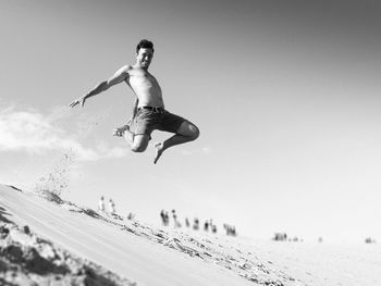 Full length of shirtless man jumping on beach against clear sky