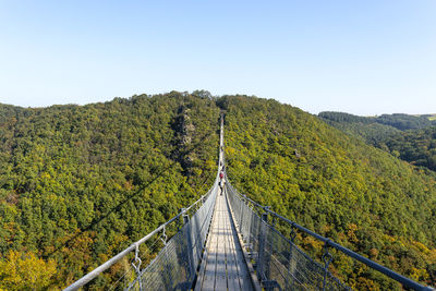Suspension wooden bridge with steel ropes over a dense forest in west germany, visible tourists. 