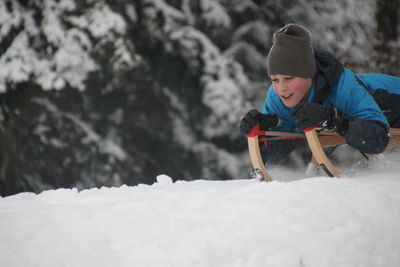 Boy tobogganing on snow covered landscape