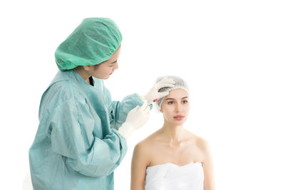 Female doctor injecting examining patient with botulinum toxin injection against white background