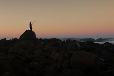 Silhouette man standing on rock against sky at sunset