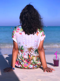 Rear view of woman sitting at beach against clear sky