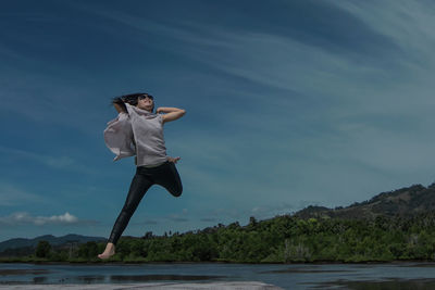 Full length of young woman jumping against sky