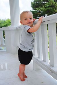 Portrait of baby boy standing by railing in balcony