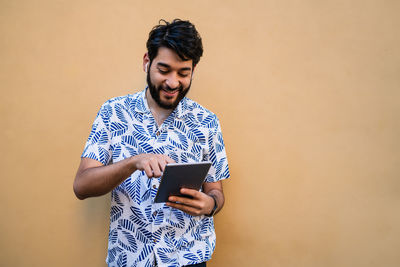 Young man using digital tablet while standing by wall outdoors
