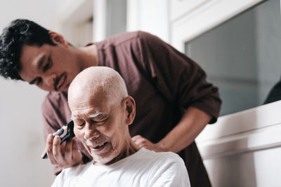 Close-up of grandson cutting senior man hair at home