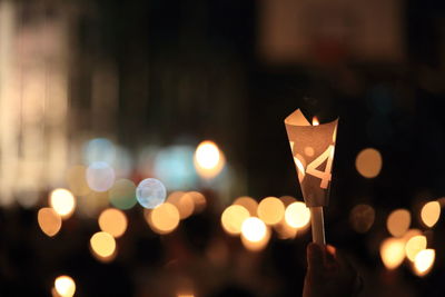 Close-up of hand holding illuminated candle at night