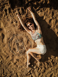 Full length of woman lying by bitcoin symbol at beach