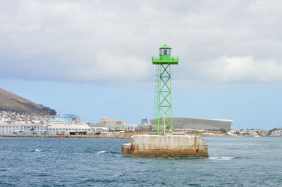 Lighthouse amidst sea and buildings against sky