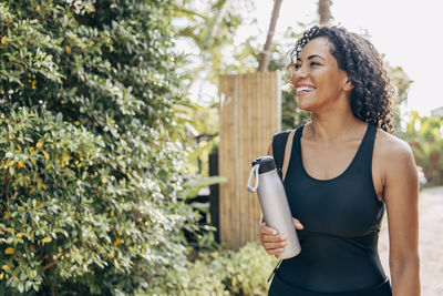Happy mature woman looking away while holding water bottle at wellness resort
