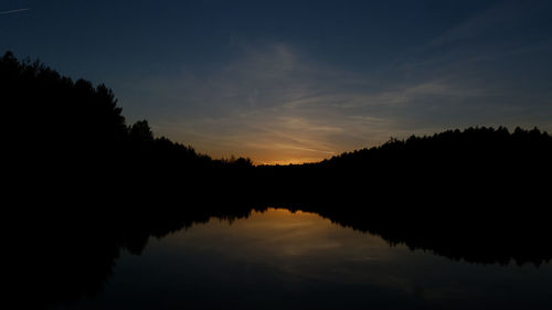 Silhouette trees by lake against sky during sunset