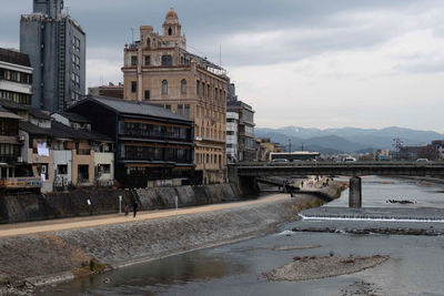 Bridge over kamo river by buildings in city against sky