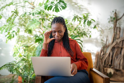 Young woman using mobile phone while sitting against plants