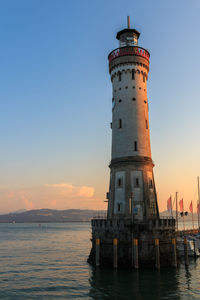 Lighthouse by sea against sky during sunset