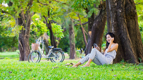 Smiling young woman listening music on headphones while sitting at park