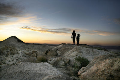 Rear view of silhouette people standing on rock against sky during sunset