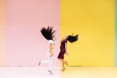 Side view of women dancing while standing against colored wall