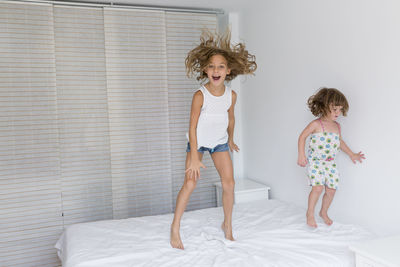 Portrait of happy girl with sister jumping on bed at home