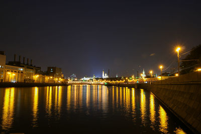 Illuminated buildings by river against sky at night