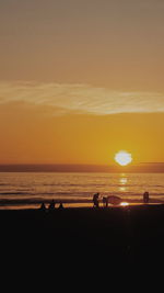 Silhouette people on beach against sky during sunset