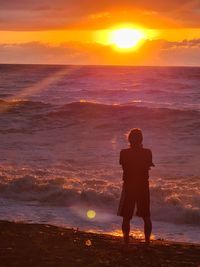 Rear view of man standing on beach during sunset