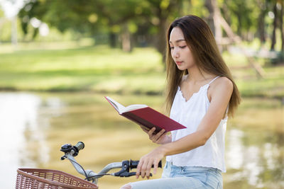 Beautiful woman reading book on bicycle by lake