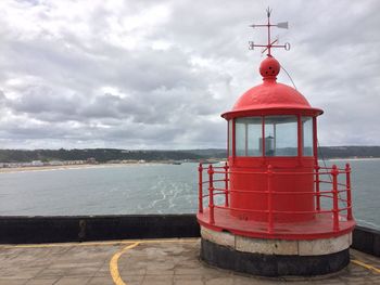 Red lighthouse by sea against sky
