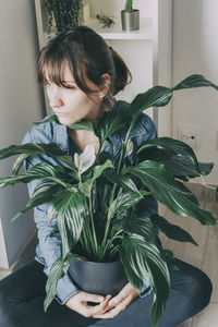 Portrait of a woman with brown hair sits on the floor of her house and hugs a plant from a pot