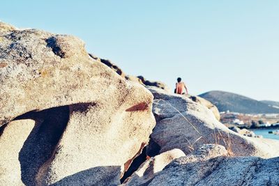 People on rocks against clear sky