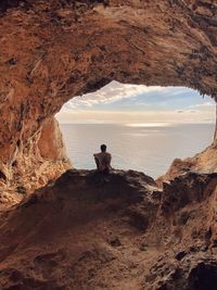 People sitting on rock by sea against sky