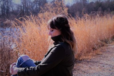 Side view of woman sitting by plants on field