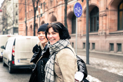 Portrait of cheerful young women wearing warm clothing while standing on street in city during winter