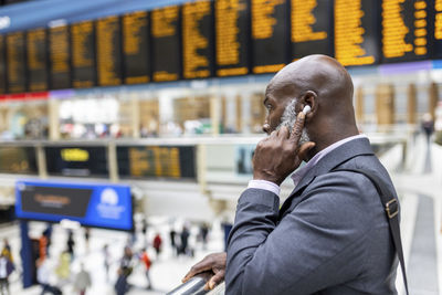 Businessman touching wireless in-ear headphones at railroad station