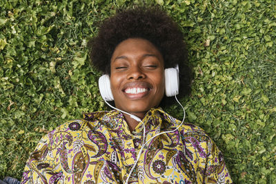 Smiling woman listening music through headphones while lying on grass